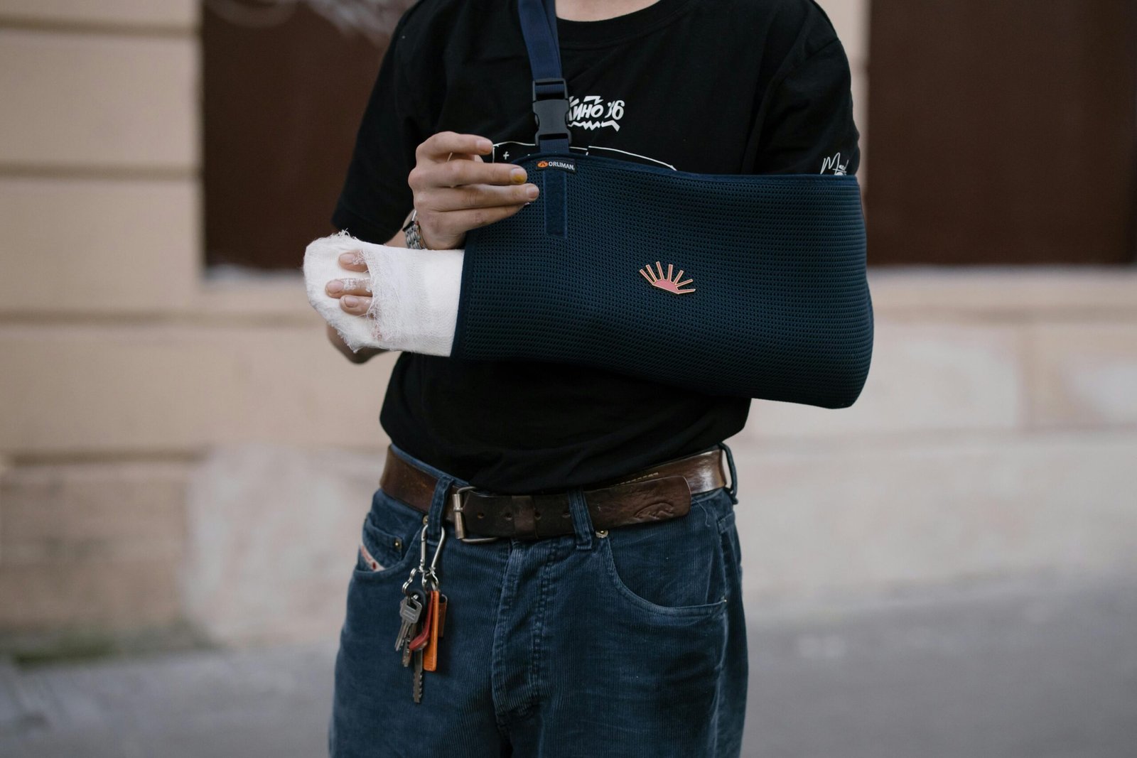 A man wearing a dark sling with a bandaged arm, standing outdoors in casual attire.